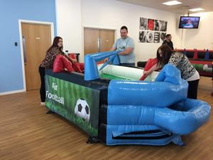 Three people playing blow football at an indoor football themed event.