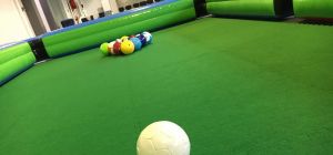 Giant footballs set up for a game of Football Pool at an indoor event. The footballs are on a large astroturf pitch with an inflatable surround.