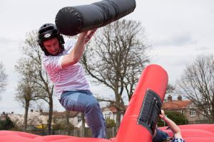 A man playing on the inflatable gladiator joust who has just been hit off the rocking podium.