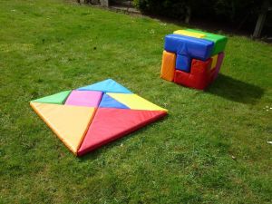 Giant Tangram and Soma Cube puzzles set up at a team building event on a grass surface.